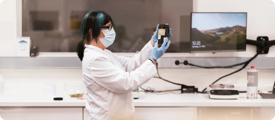 mitarbeiterin-labor-startseite-cannabis-apotheke Eine Mitarbeiterin der Cannabis Apotheke inspiziert im Labor ein Braunglas mit medizinischem Cannabis.